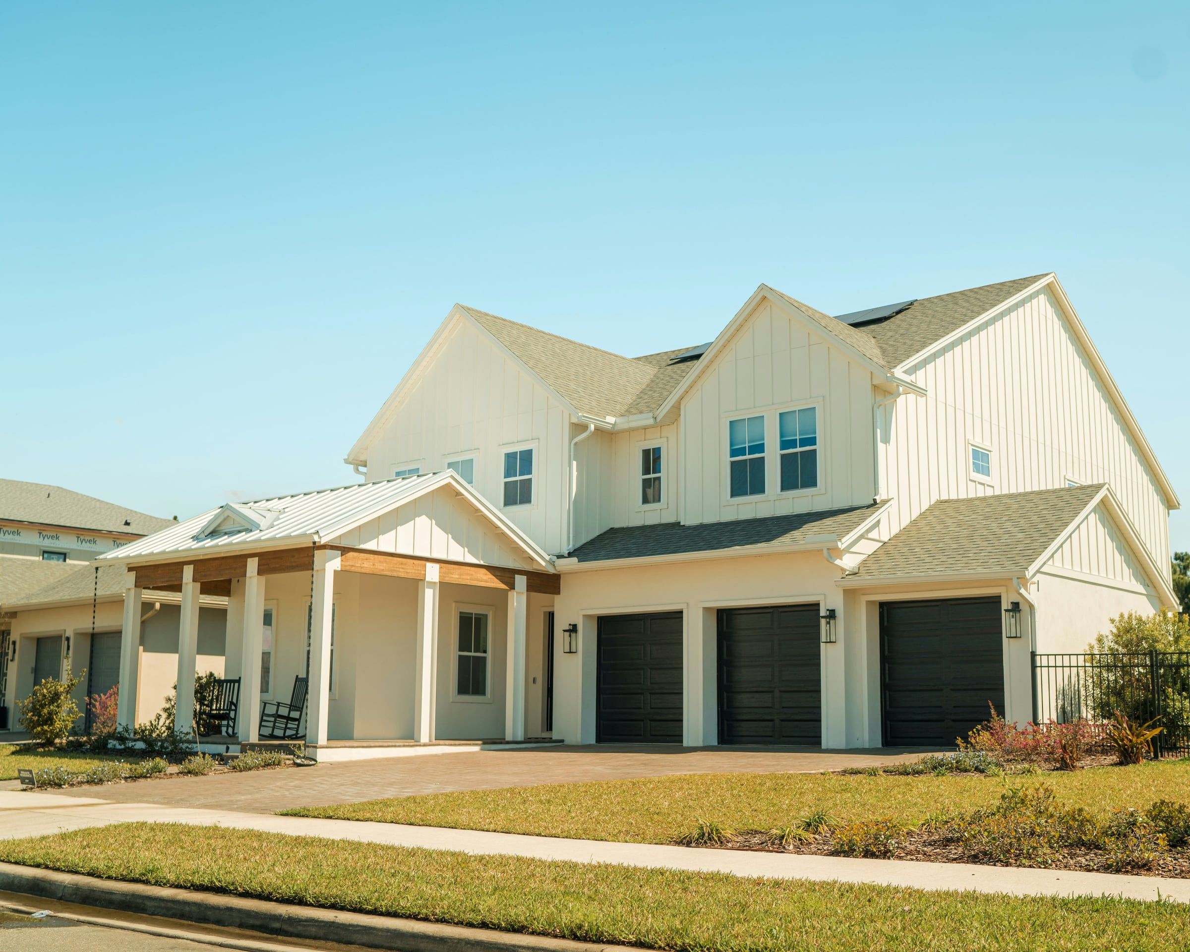 Two-story white house in Orlando, Florida, with a tan architectural asphalt shingle roof over the main house and a metal roof over the front porch